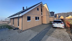 A modern two-story house with a sloped roof, a driveway, and a parked car. - Ferienhaus im Skandinavischen Stil (Mirow)