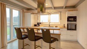 A modern kitchen with a central island, bar stools, a microwave, and a built-in oven. - Ferienhaus im Skandinavischen Stil (Mirow)