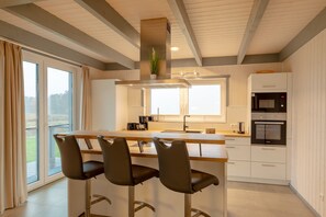 A modern kitchen with a central island, bar stools, a microwave, and a built-in oven. - Ferienhaus im Skandinavischen Stil (Mirow)