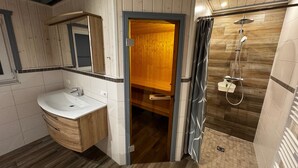 A modern bathroom with a wooden vanity, a shower enclosure, and a mirror. - Ferienhaus im Skandinavischen Stil (Mirow)