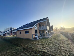 Une maison moderne à deux étages, dotée d’un balcon, d’un toit plat et surplombant un ciel dégagé.