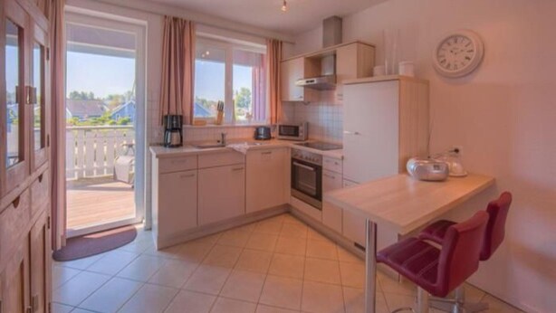 A compact kitchen with a dining area, a view through the window, and a clock on the wall. - Appartement im Ferienpark in Rechlin (Rechlin)