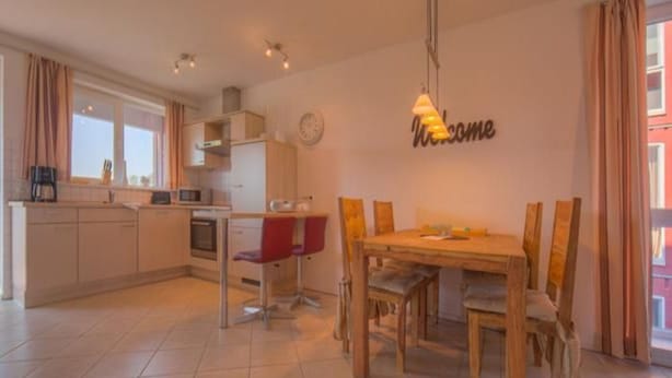 A modern kitchen with a dining area, a clock on the wall, and a 'Welcome' sign. - Appartement im Ferienpark in Rechlin (Rechlin)