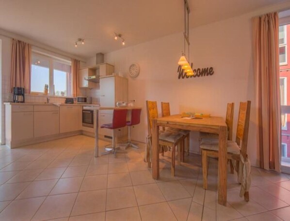 A modern kitchen with a dining area, a clock on the wall, and a 'Welcome' sign. - Appartement im Ferienpark in Rechlin (Rechlin)