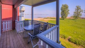 A covered outdoor area with a table and chairs, overlooking a beach and grassy landscape. - Appartement im Ferienpark in Rechlin (Rechlin)