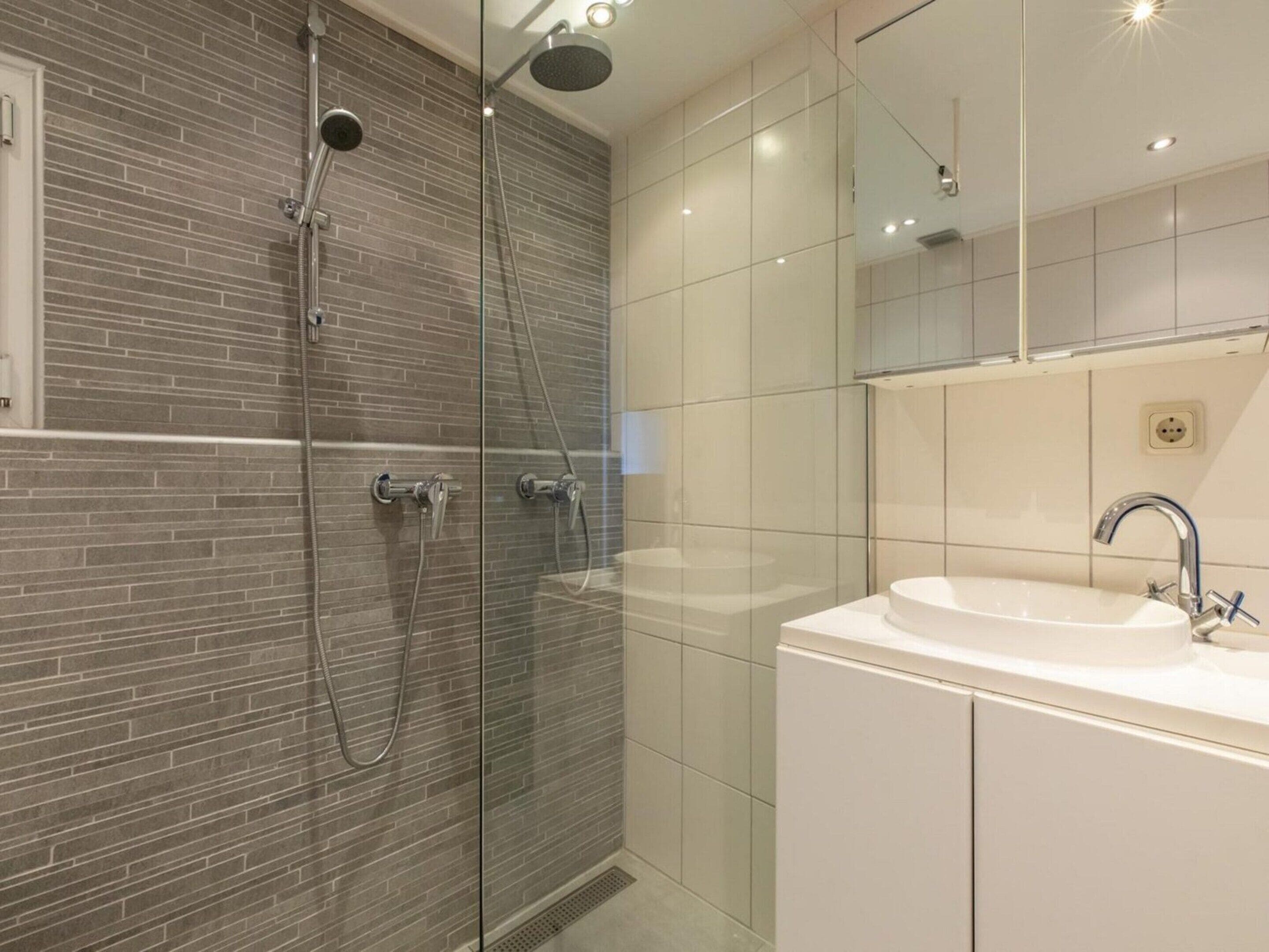 Un baño moderno con ducha de vidrio, un lavabo blanco y un espejo sobre el lavabo.