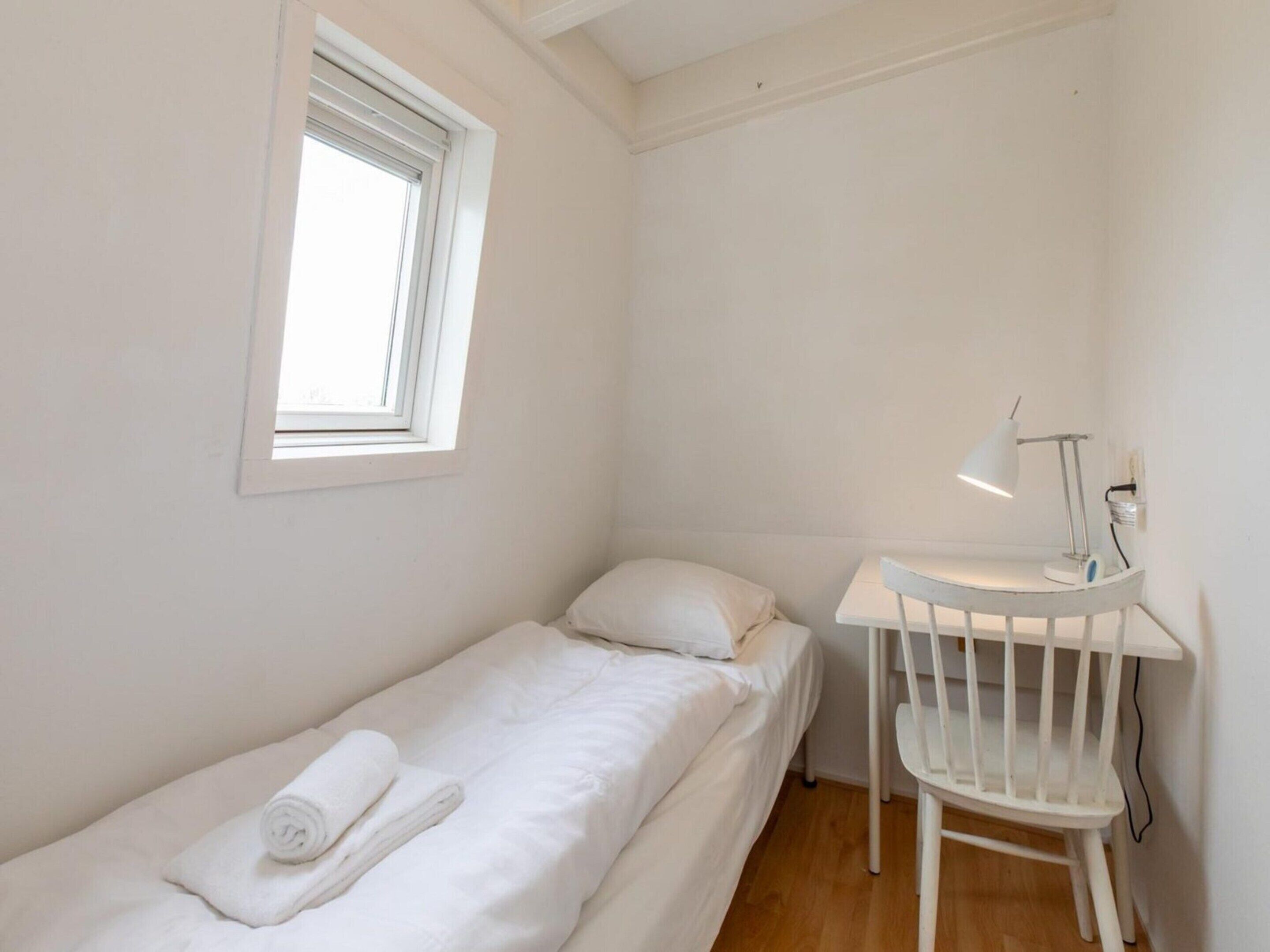 A single-bed room with a window, a desk with a chair, and a lamp.