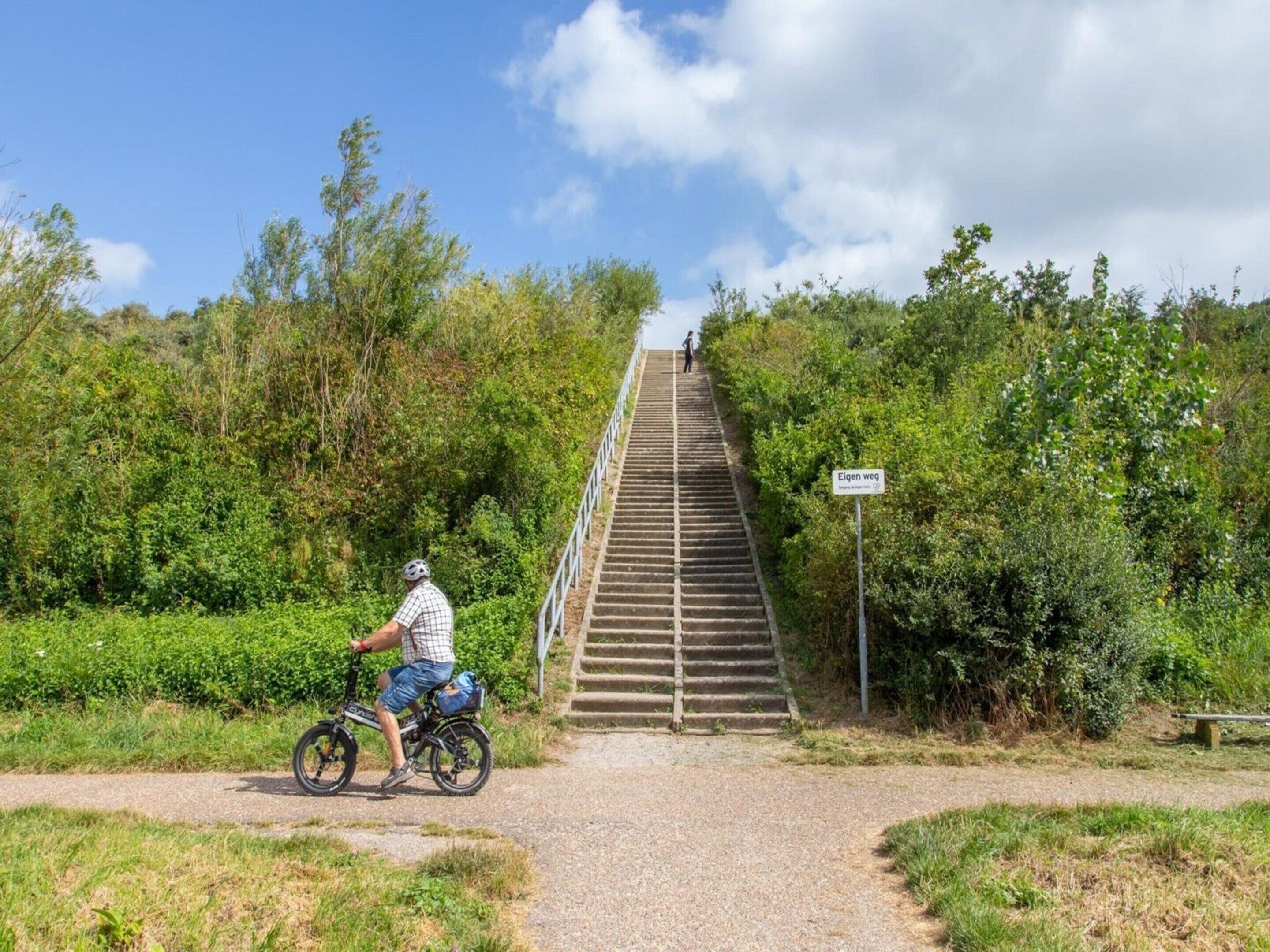 A man on a bicycle at the base of a staircase surrounded by greenery.