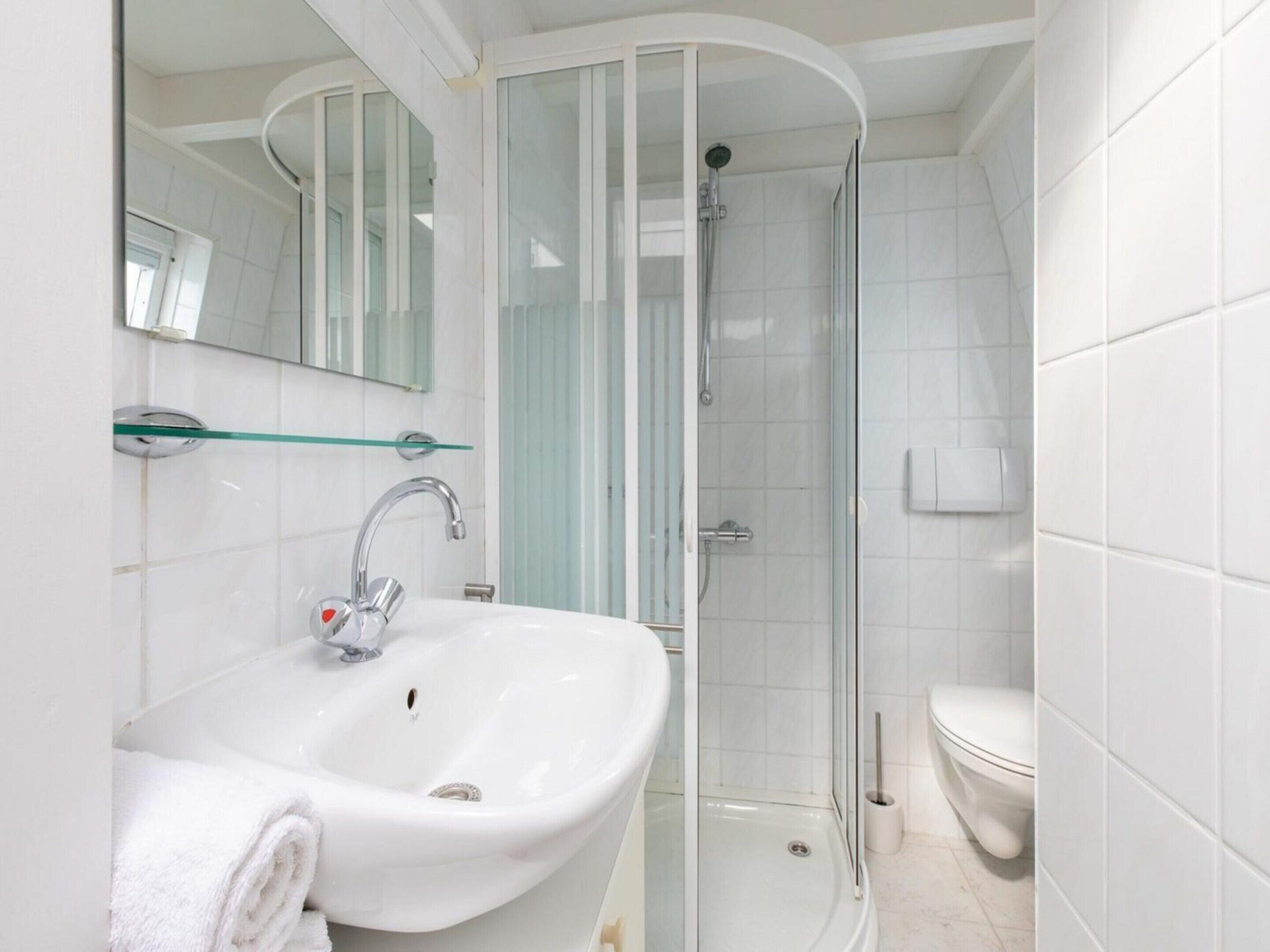 Un baño con lavamanos blanco, cabina de ducha con mampara de vidrio y un inodoro.