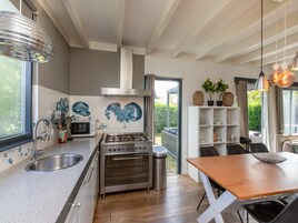 Una cocina moderna con estufa a gas, horno y pileta de acero inoxidable. Hay un comedor con mesa y sillas de madera.