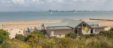 Un bâtiment situé sur la côte, doté d’un toit végétalisé, et qui se trouve près d’une plage de sable, avec vue sur la mer.
