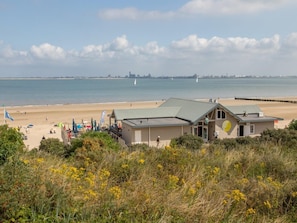 A coastal building with a green roof, situated near a beach with a sandy shore and a view of the sea.
