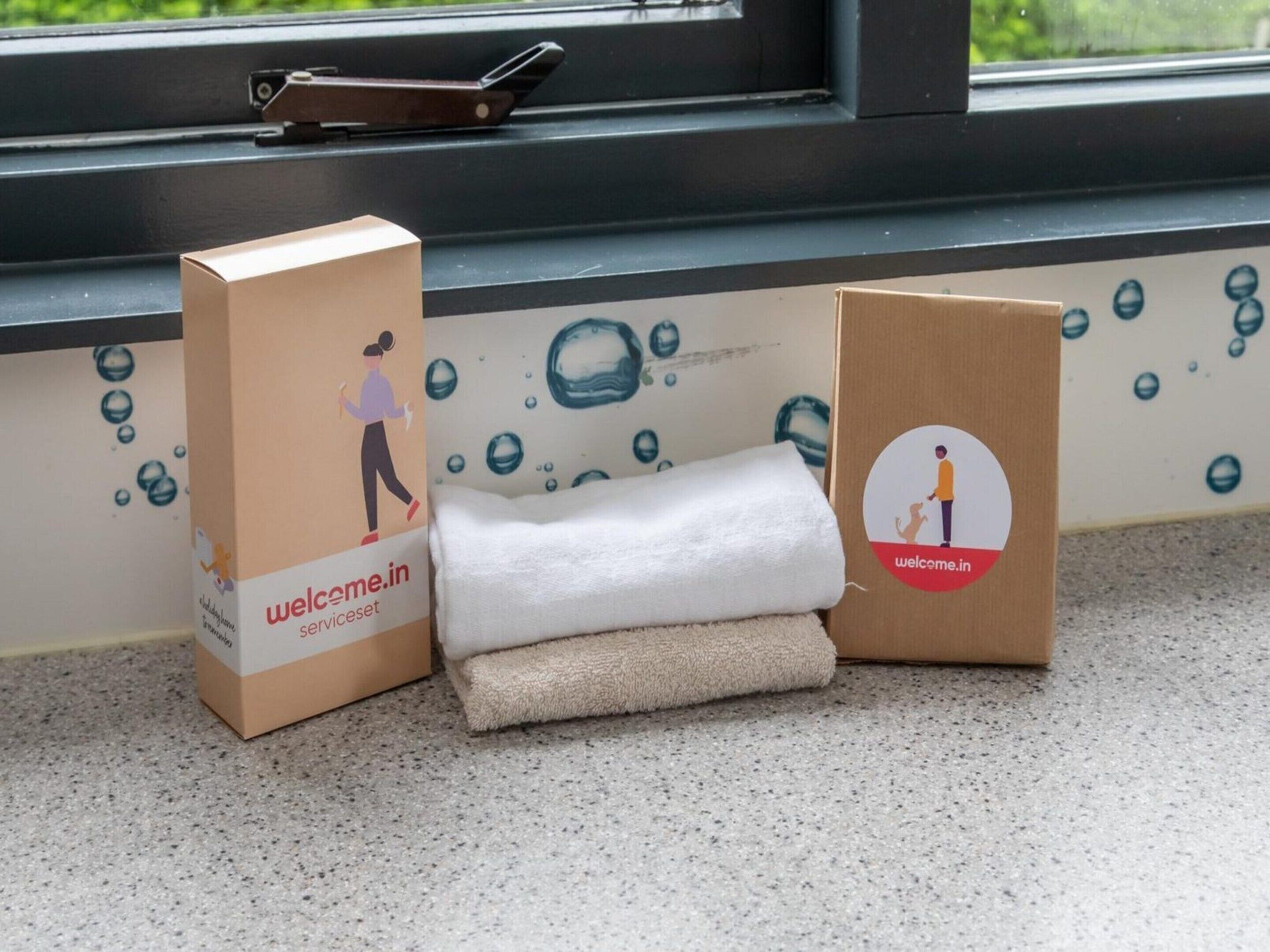 Dos cajas de cartón con la marca 'welceme.in', una ventana con vistas y una toalla en el suelo.