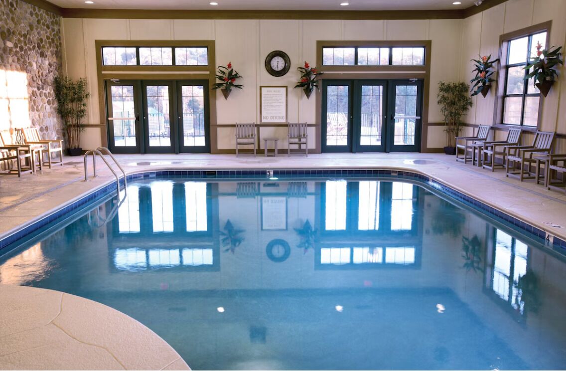 Una piscina interior con suelo de baldosas, dos puertas y una zona de estar con sillas.