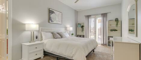 A bedroom with a bed, nightstands, a dresser, a ceiling fan, a window with curtains, and a wall-mounted shelf with plants.