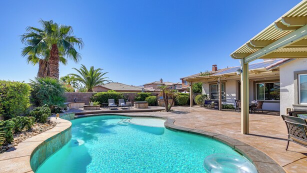 Una piscina con borde curvo, rodeada por un patio con mobiliario exterior y una pérgola.
