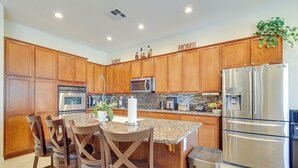 Una cocina con armarios de madera, electrodomésticos de acero inoxidable, encimera de granito y una isla central con taburetes de bar.