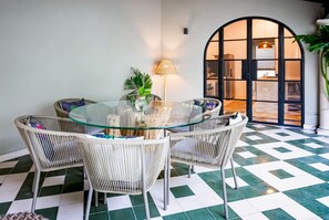 Un comedor con una mesa de vidrio rodeada de sillas de mimbre, una lámpara y una planta en maceta.