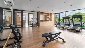 Un gimnasio moderno con equipo de ejercicio, suelo de madera y ventanas amplias que dan a zonas verdes.
