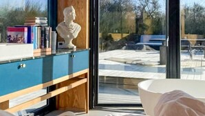 A room with a large window, a bust sculpture on a wooden cabinet, and a view of an outdoor area with a bench and trees. - Chic Retreat in Sjaellands Odde - By Traum Ferienwohnungen (Sjællands Odde)