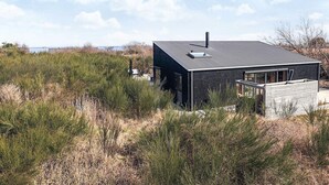 A modern house with a flat roof, large windows, and a chimney, surrounded by tall grasses and a clear sky. - Chic Retreat in Sjaellands Odde - By Traum Ferienwohnungen (Sjællands Odde)