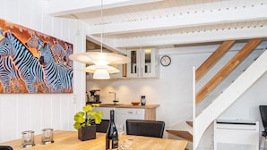 Et moderne køkken med hvide skabe, et spiseområde med et træbord, og en trappe, der fører op til et andet niveau.
