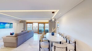 Una sala de estar moderna con un sofá, una mesa de comedor con sillas estampadas y un ventanal con vistas a edificios.