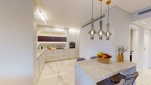 Una cocina moderna con muebles blancos, encimera de mármol y una isla central con cesta de fruta.