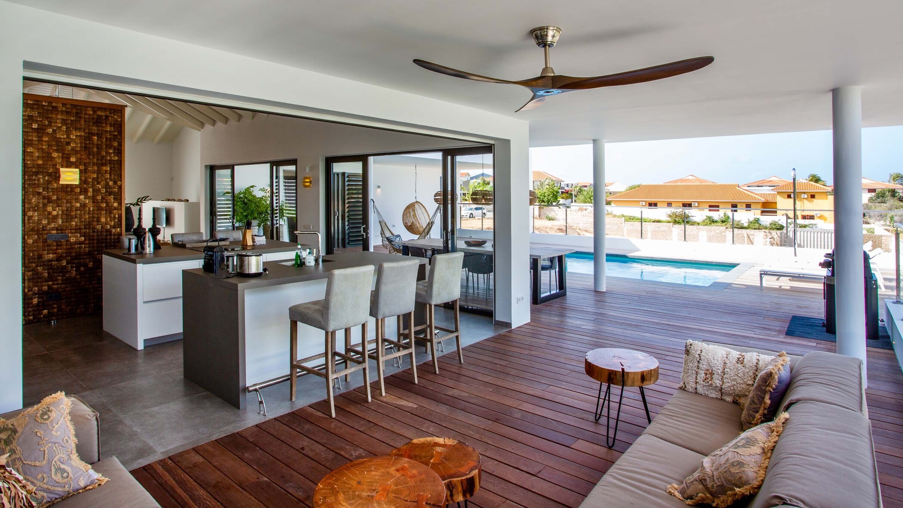 A modern open-plan living area with a kitchen, dining space, and a view of a pool.
