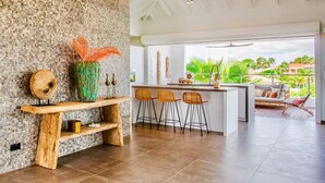 A modern kitchen with a rustic wooden bench, a green vase, and a bar area with stools. - The Villas by LXRYHOME (Jan Thiel)