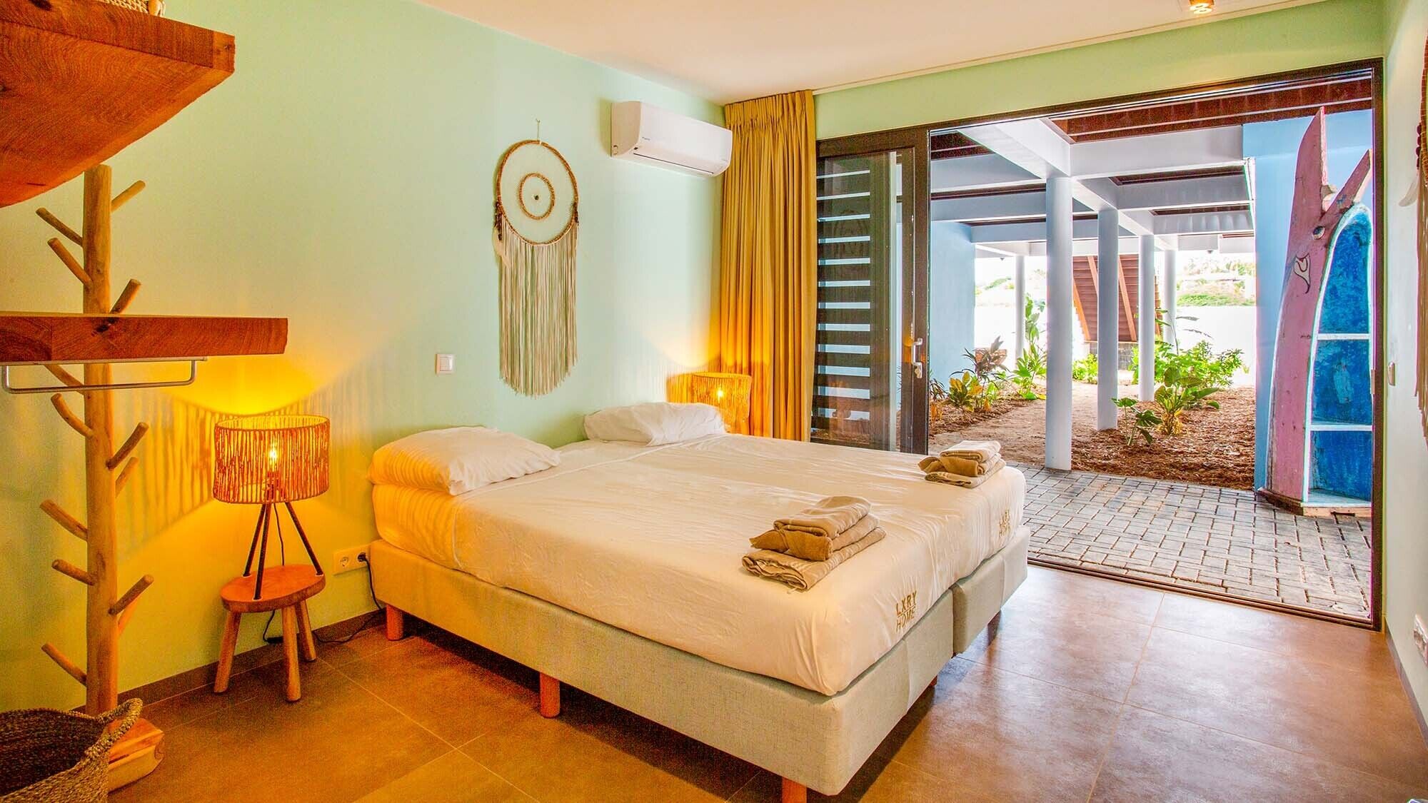 A bedroom with a bed, bedside lamps, a dreamcatcher, and a view of the outdoors.