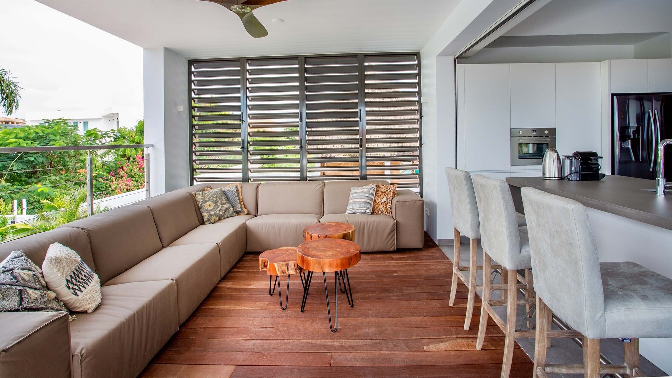 A modern living area with a sofa, round wooden tables, and a kitchen area with bar stools.