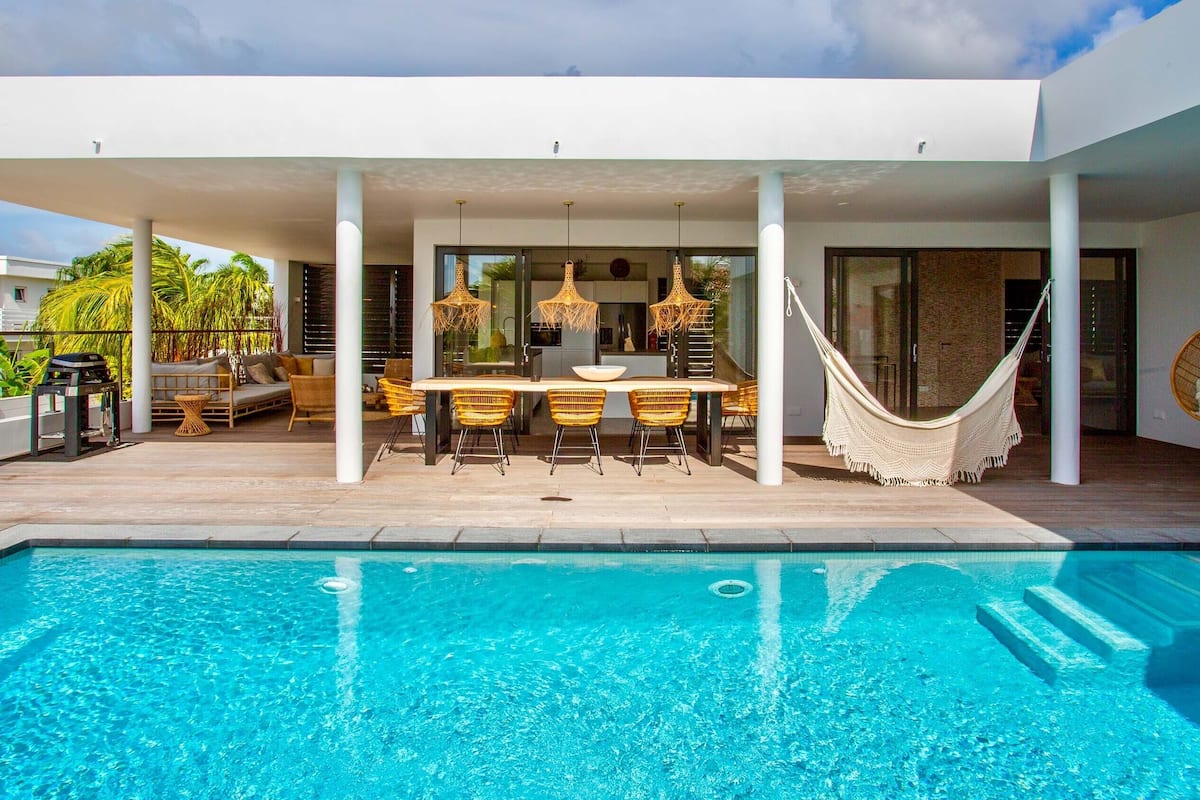 Un área de piscina moderna al aire libre con zona de comedor y una hamaca.