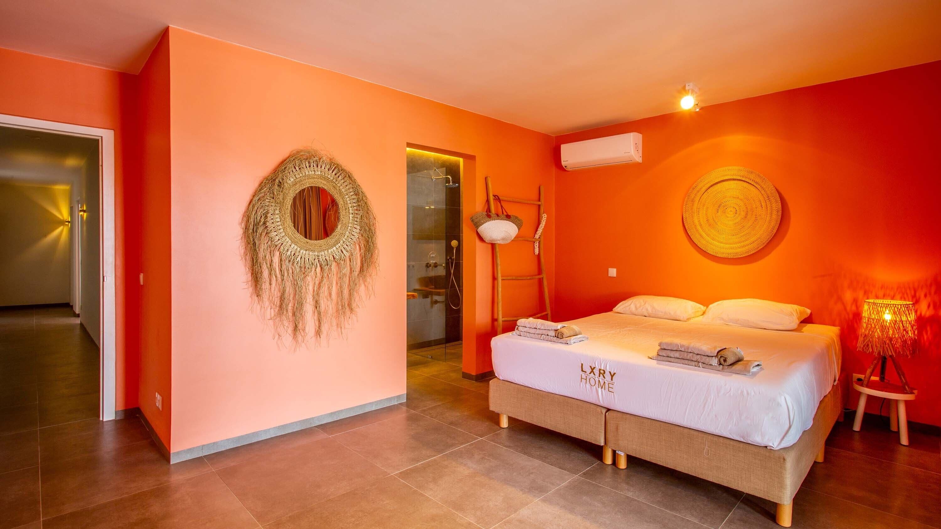 A bedroom with a bed, a wall-mounted air conditioner, a woven wall hanging, and a woven lamp.