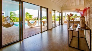 A spacious indoor area with a pool view, a hammock, and a dining area with a table and chairs. - The Villas by LXRYHOME (Jan Thiel)