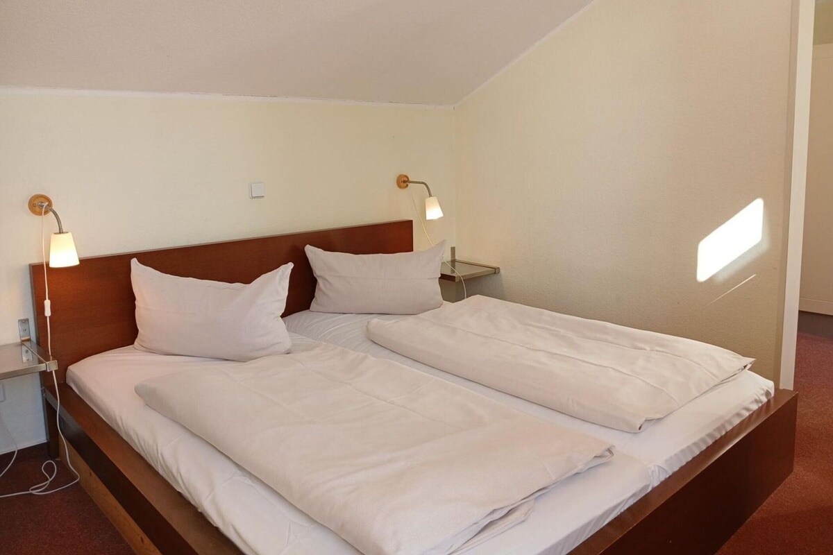 A twin bed with two pillows, a wooden headboard, bedside tables with lamps, and a small window.