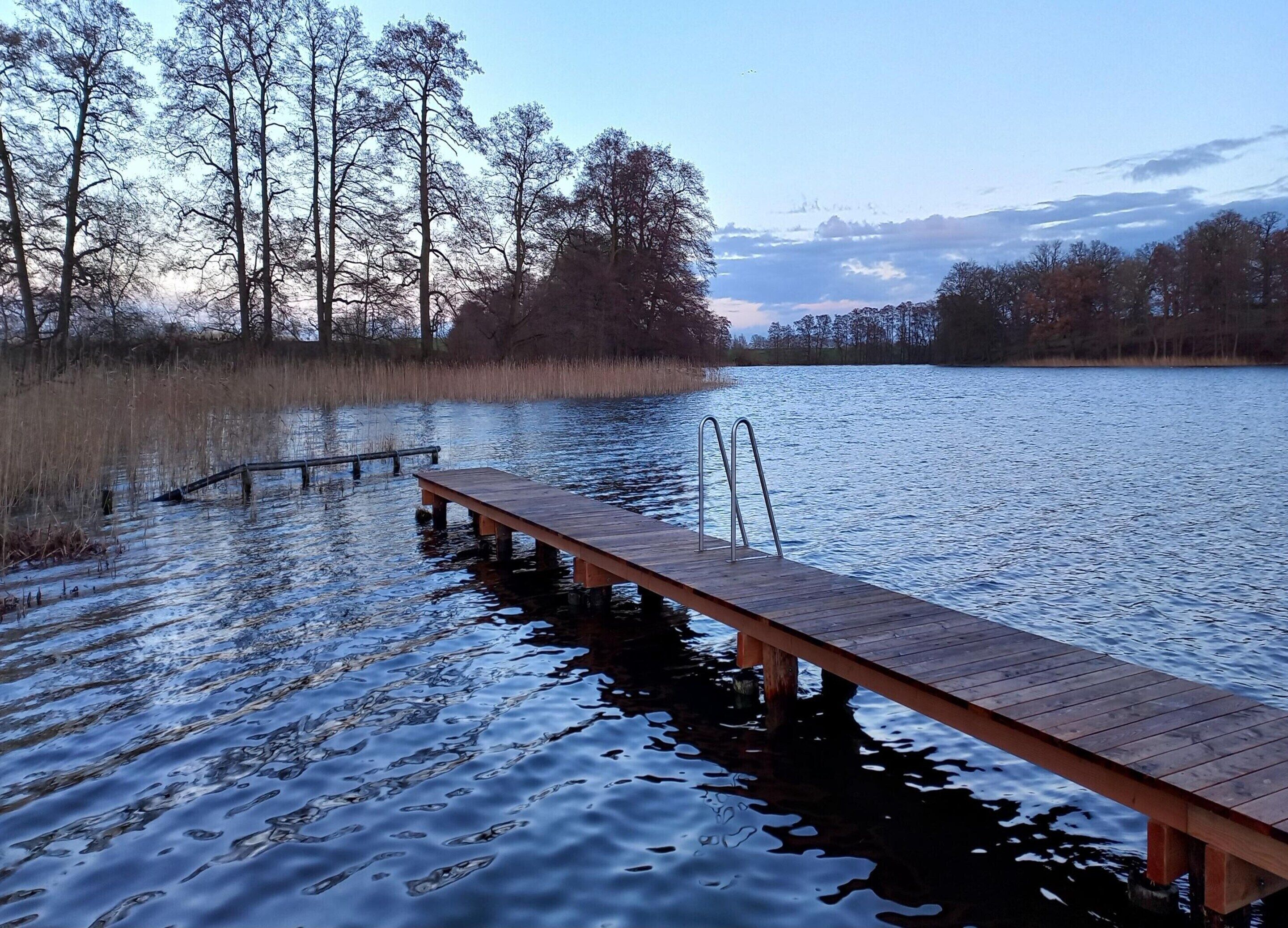 A wooden dock extending into a calm lake surrounded by trees.