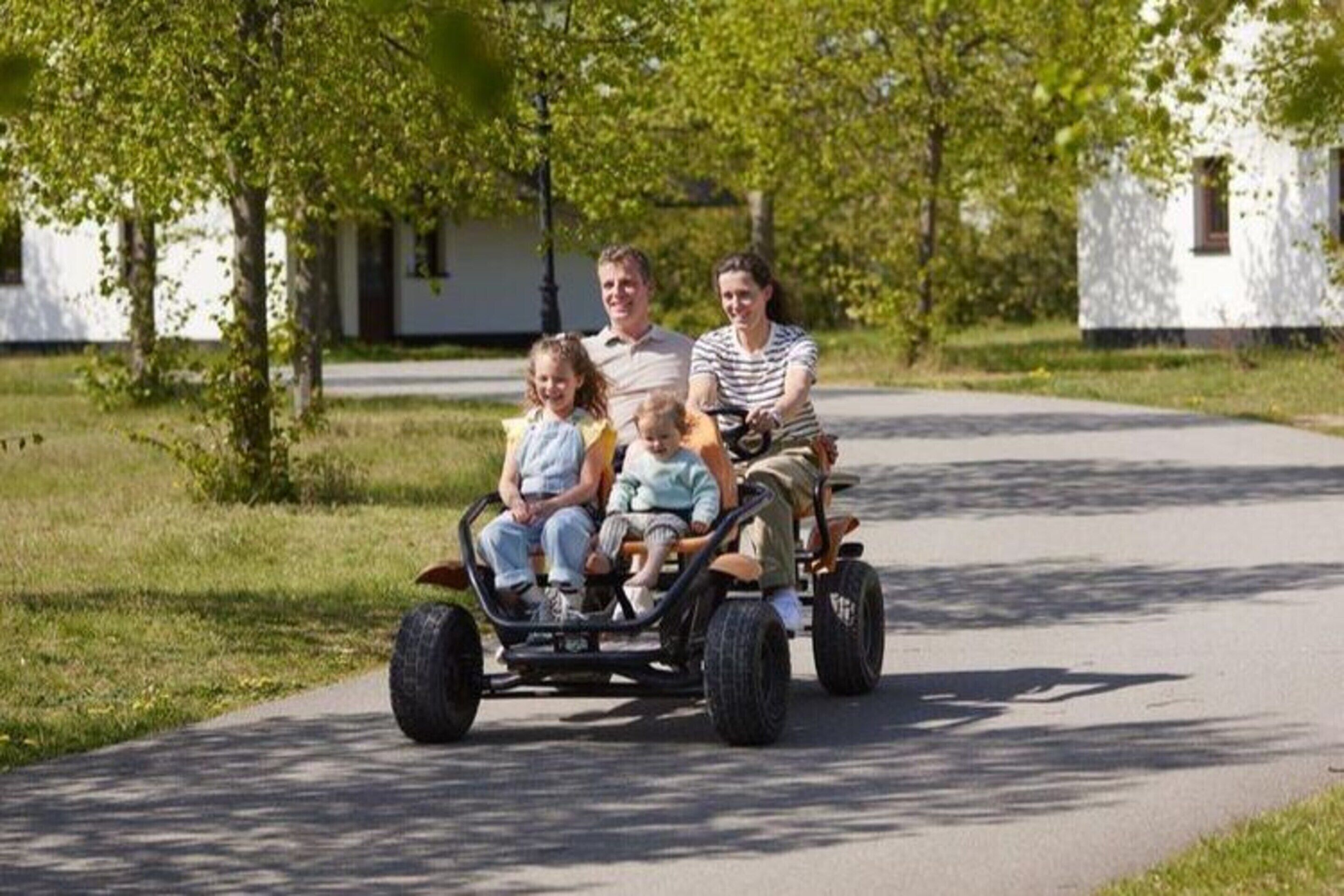 Eine Familie fährt mit einem Dreirad auf einem befestigten Weg.