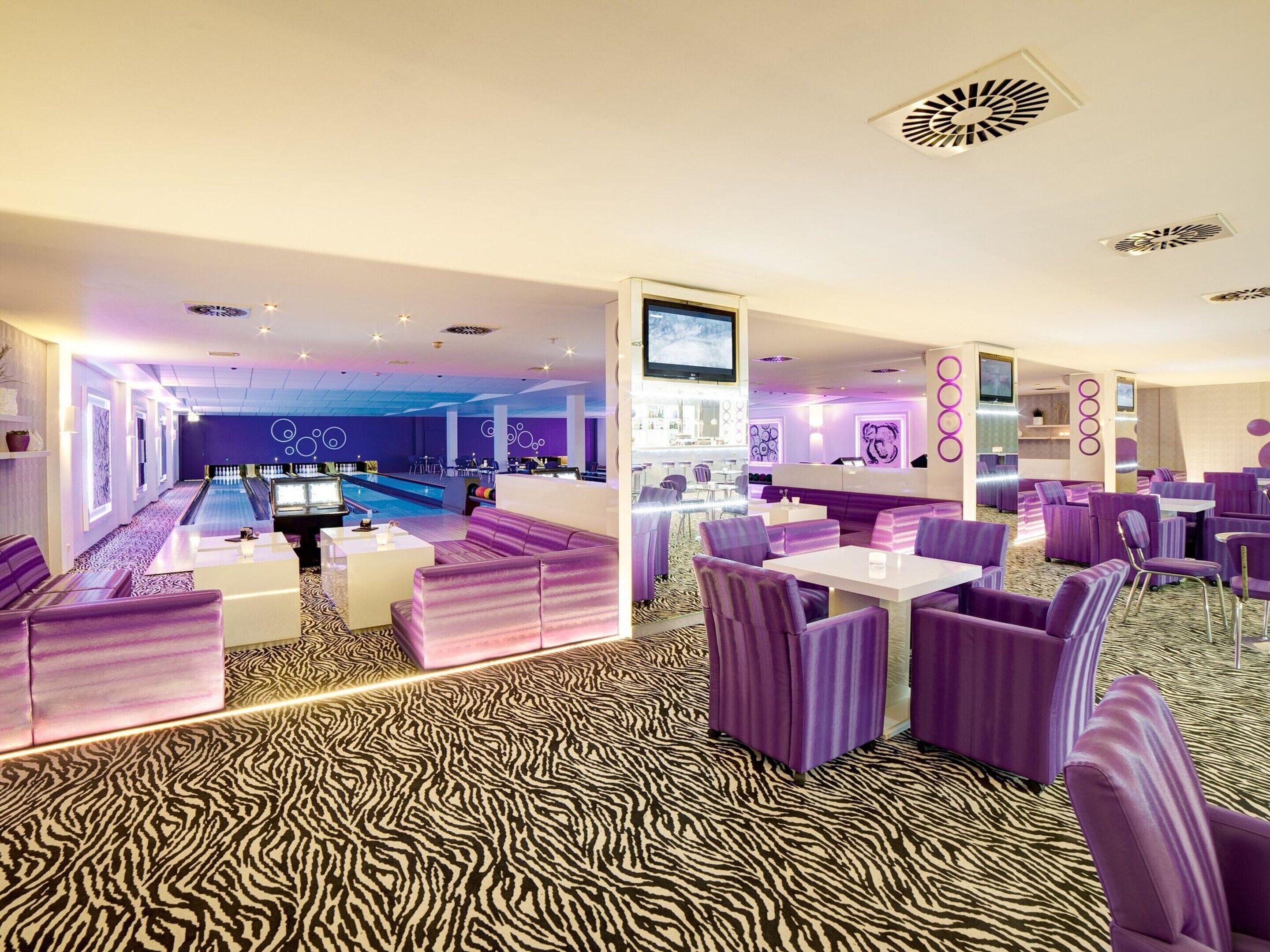 A modern lounge area with purple seating, a pool table, and a bar area.