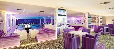 A modern lounge area with purple seating, a pool table, and a bar area.