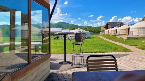 Une terrasse en bois avec un mur en verre, une chaise en métal et un banc en bois.