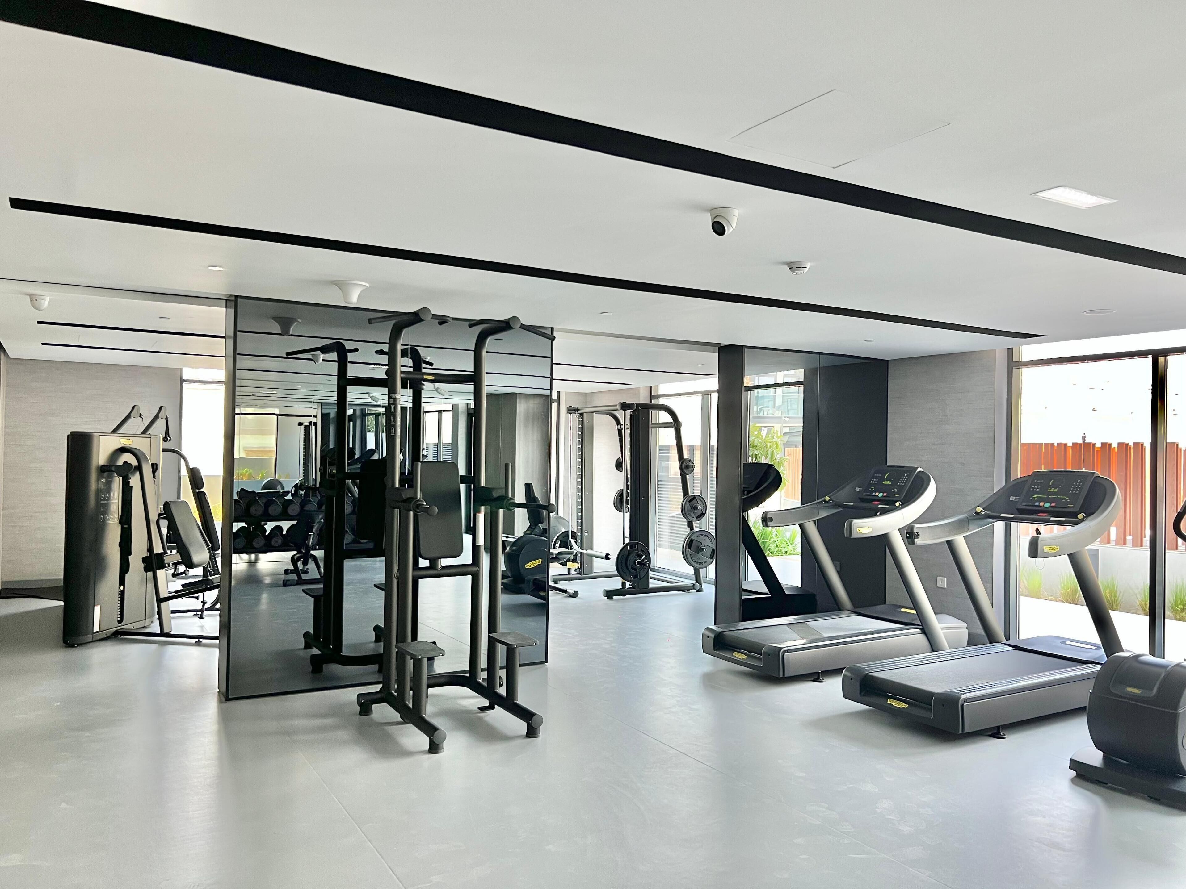 A modern gym with various exercise equipment, including a squat rack, treadmills, and weight machines.