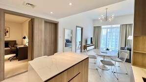 A modern hotel room with a marble-top desk, a dining area with a glass table, and a large window with curtains. - Waves - Comfortable JVC Apt with Balcony (Dubai)
