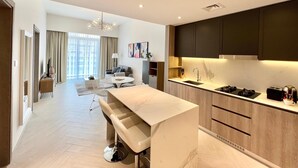 A modern kitchen with a central island, dark cabinets, and a dining area with a sofa and table. - Waves - Comfortable JVC Apt with Balcony (Dubai)