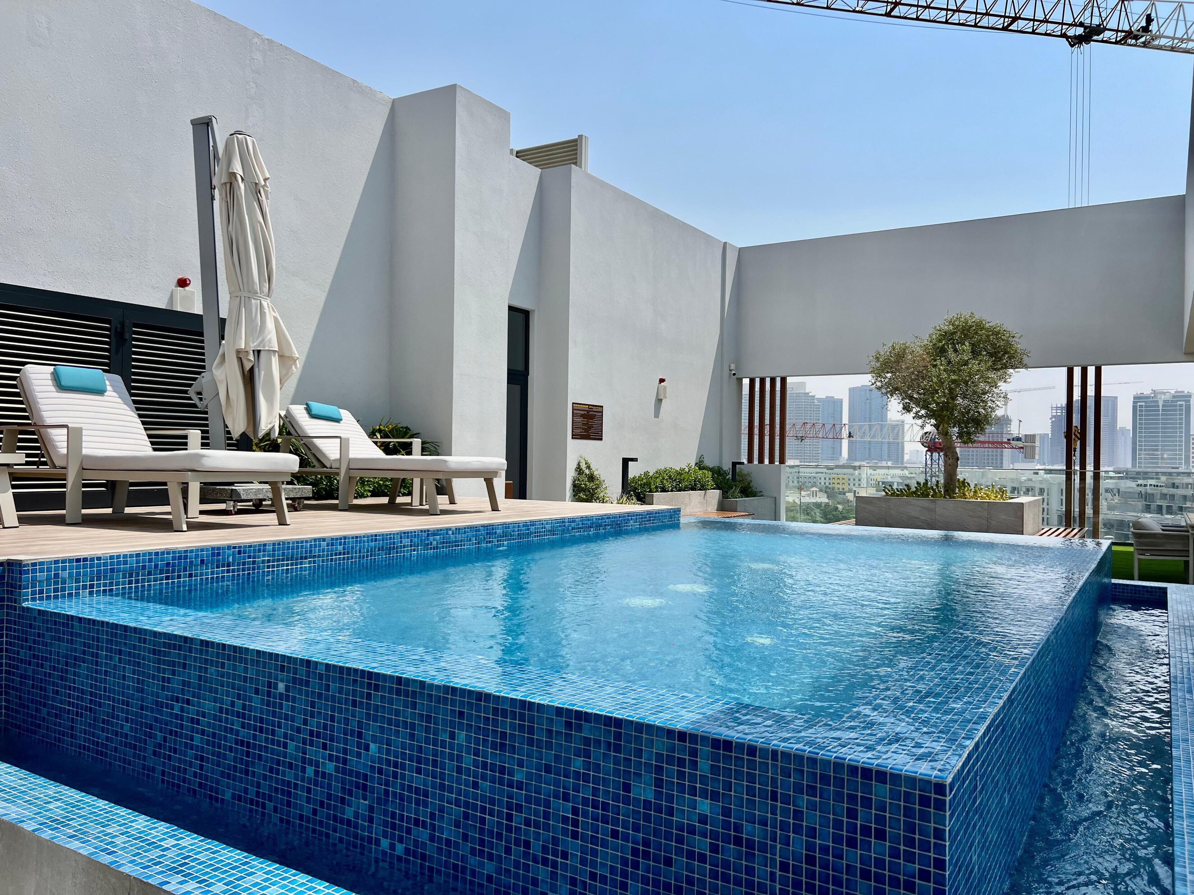 A rooftop infinity pool with lounge chairs and a city view.