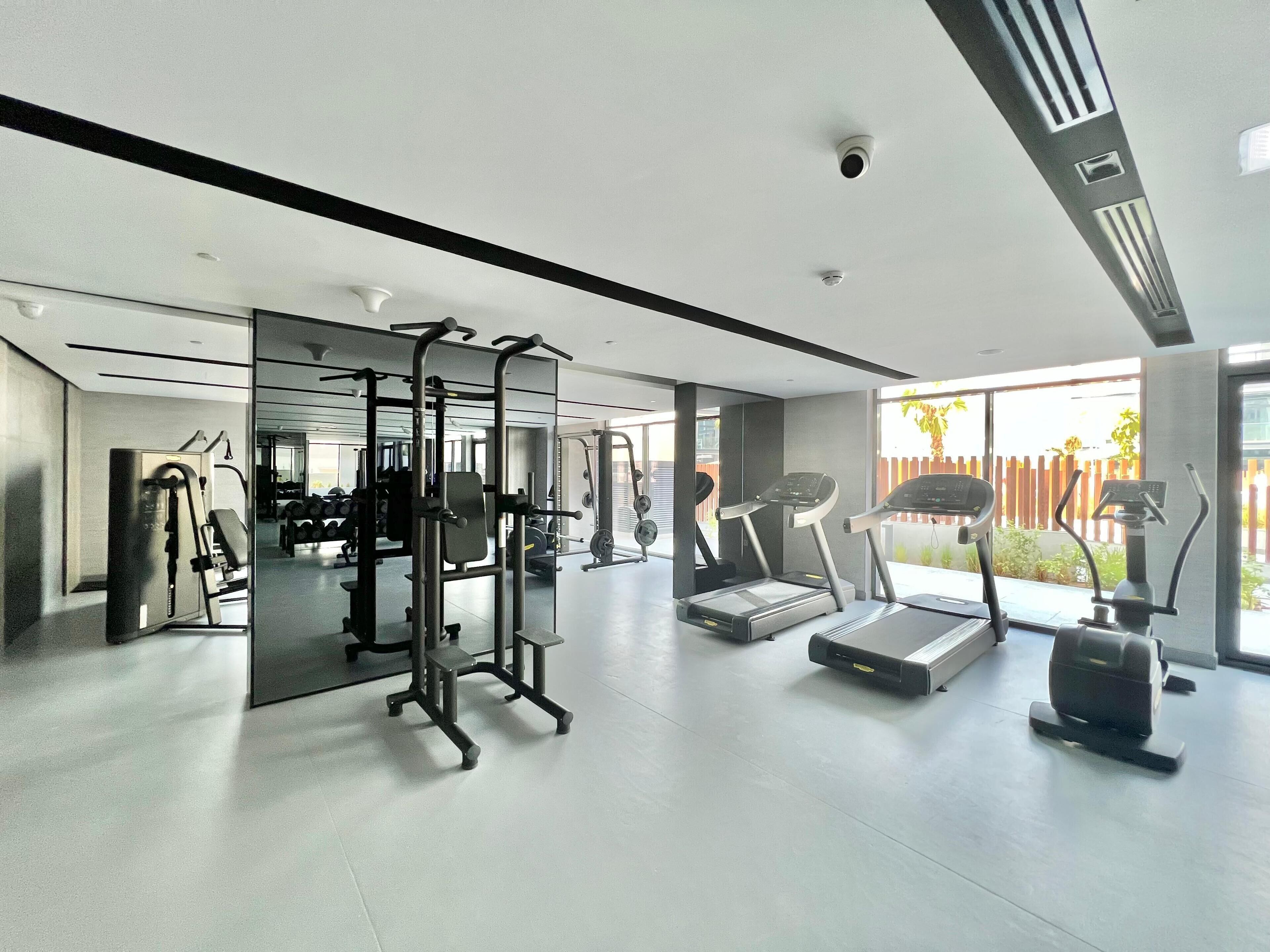 A modern gym with various exercise equipment, large windows, and a clean, spacious layout.