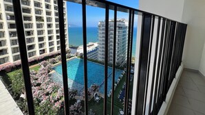 A balcony with a view of a swimming pool, a high-rise building, and the ocean. - Apartment PHONGLIEM 2 (Nha Trang)