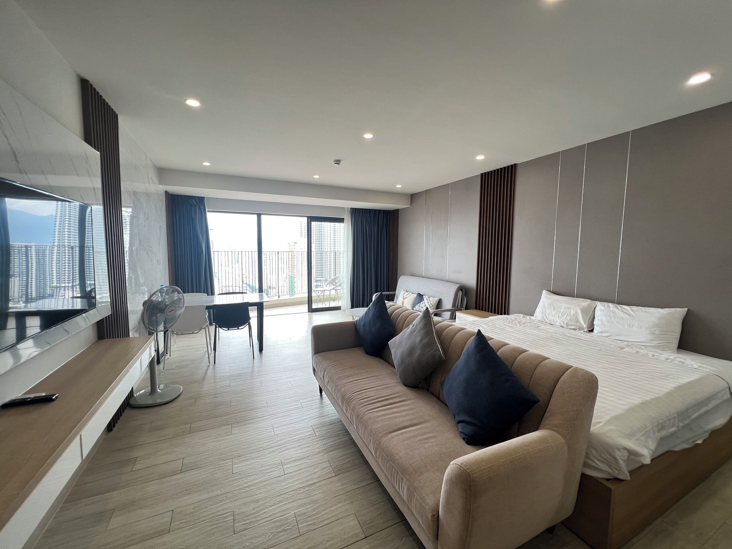 A modern hotel room with a large bed, a sofa, a TV, and a balcony with a city view.