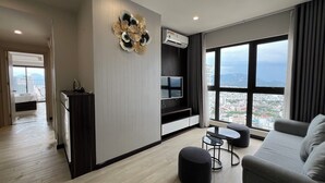 A modern living room with a large window, a flat-screen TV, a round ottoman, and a grey sofa. - Apartment PHONGLIEM 2 (Nha Trang)