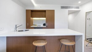 Une cuisine moderne dotée d’un îlot central, de deux tabourets, d’un évier et d’un four encastré.